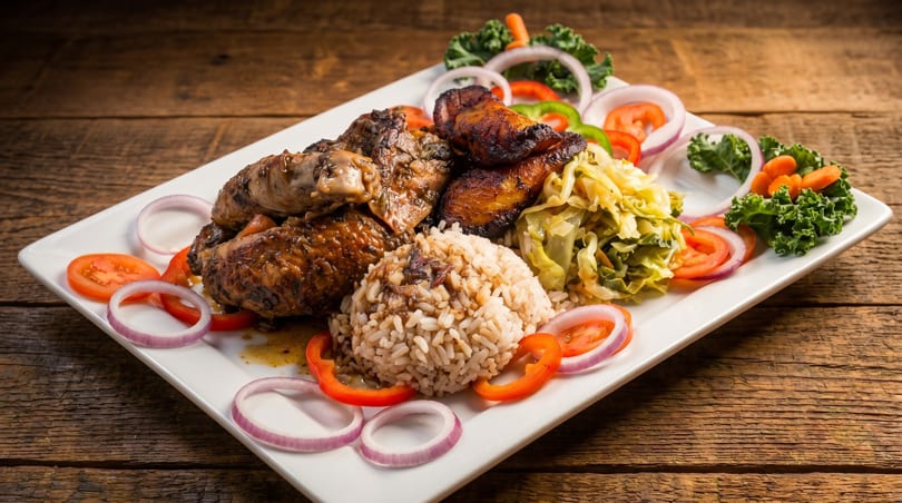 A white rectangular plate of jerk chicken, rice, and vegetables on a wooden table.